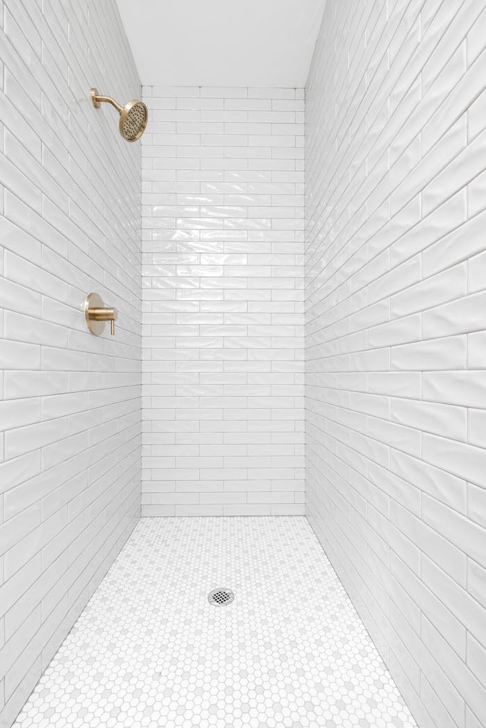 A clean, minimalist bathroom shower featuring white tiles and brass fixtures.