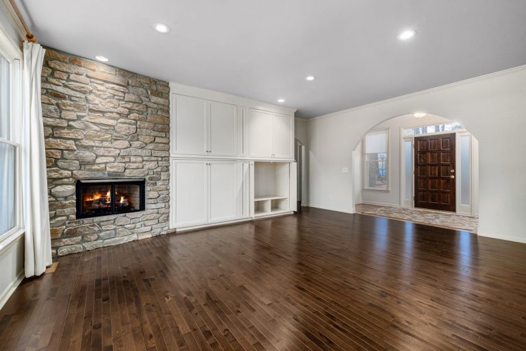 Spacious living room featuring a stone fireplace, wooden flooring, and elegant interior design.