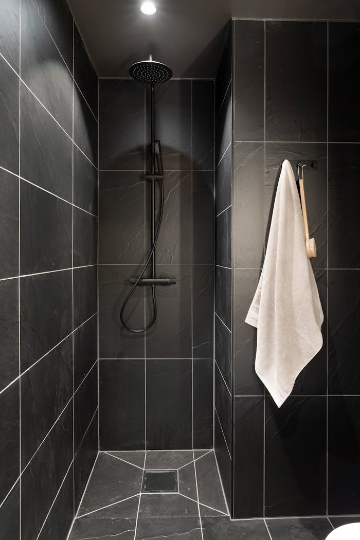 Minimalist black tiled shower with hanging white towel and modern fixtures.