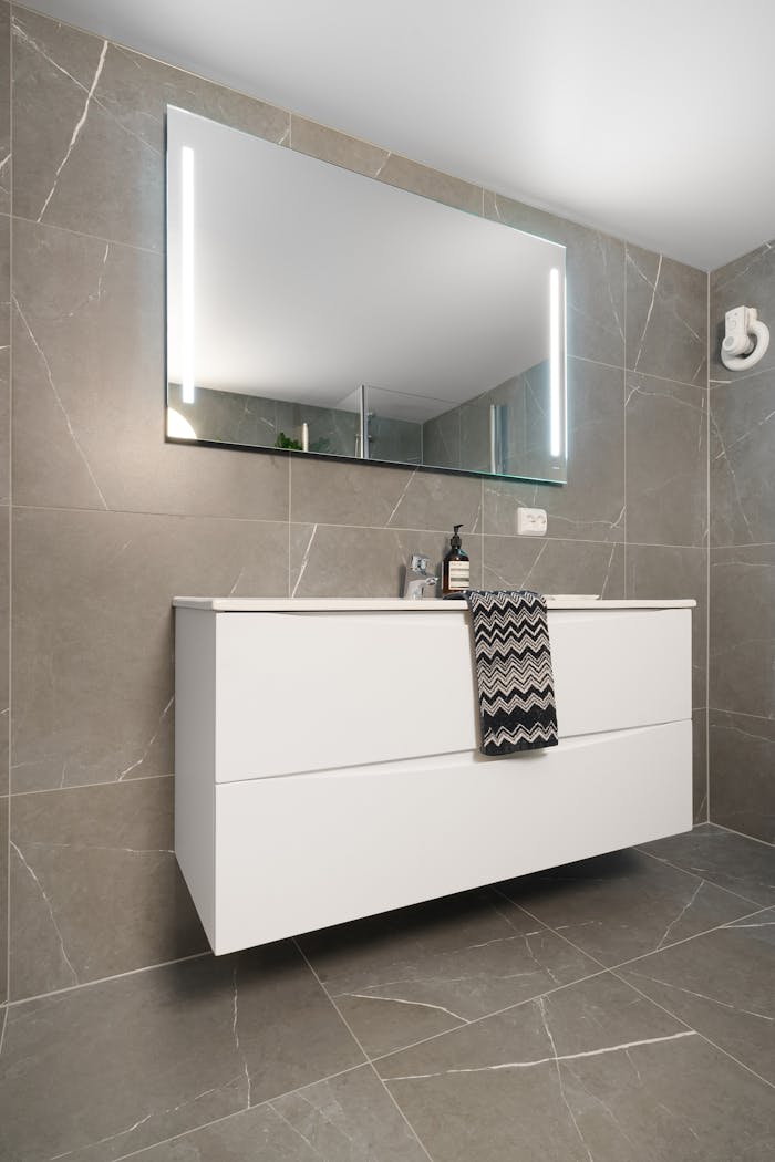 Sleek modern bathroom featuring gray tiles and illuminated mirror.