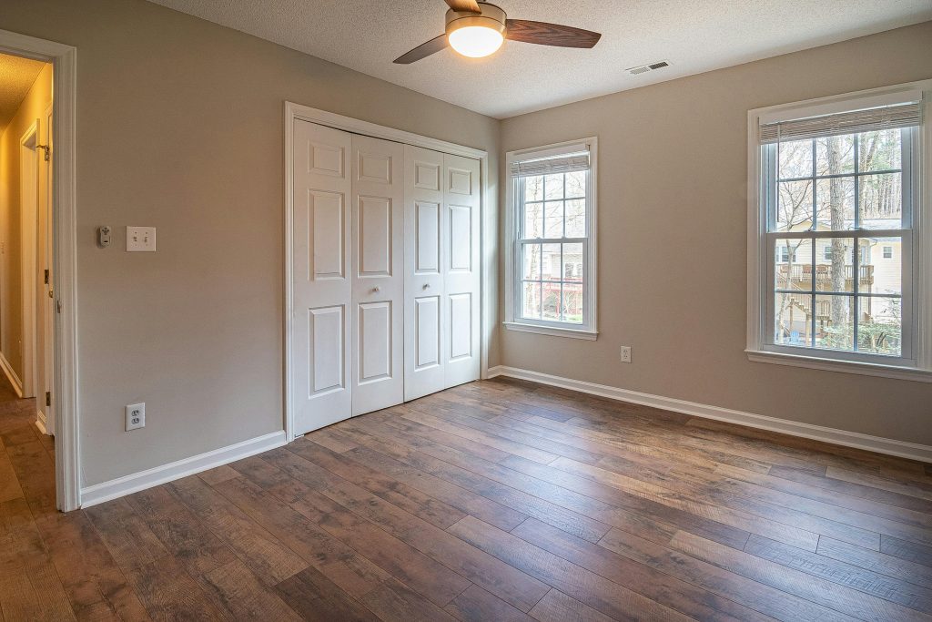 Engineered Hardwood Spacious empty room with hardwood floors, ceiling fan, and natural light from windows.