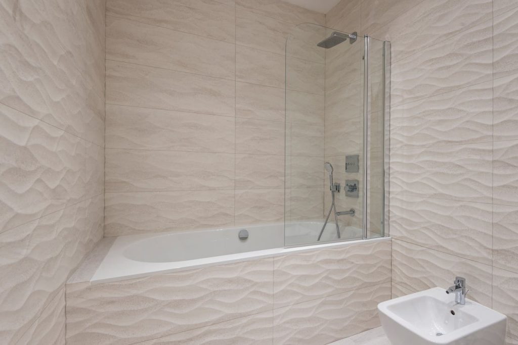 A sleek modern bathroom featuring a bathtub, shower, and beige textured tiles.