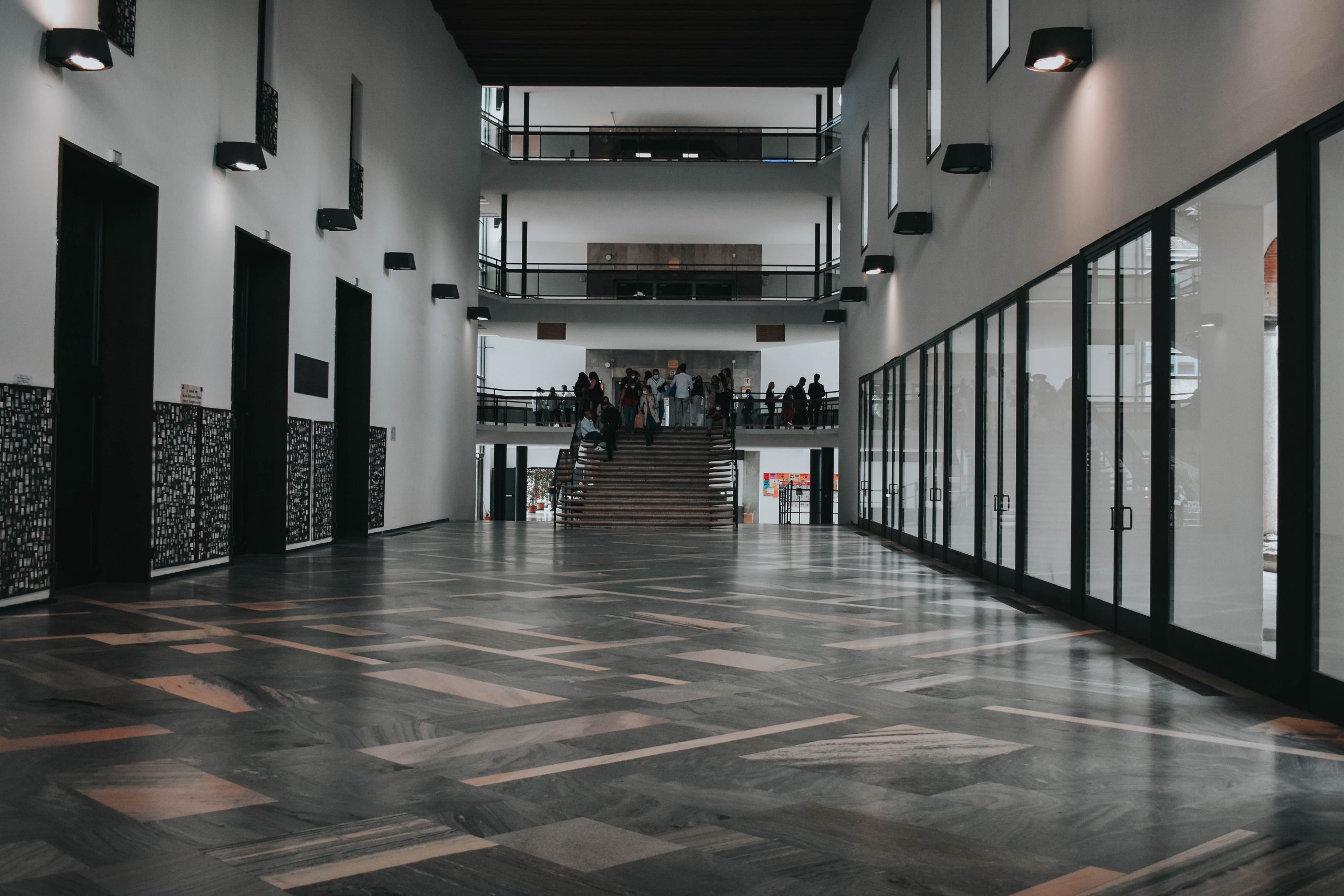 Spacious modern hall in Italy with people gathered around stairs, showcasing sleek architectural design.